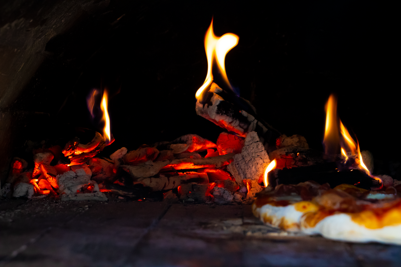 A close-up of a stone oven with bright flames, showcasing the baking process of a pizza.