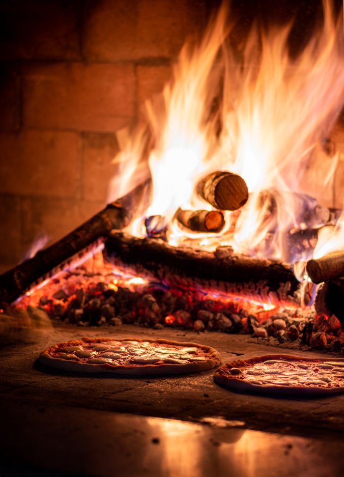 Delicious pizzas cooking in a traditional wood-fired oven, radiating warmth and flavor.
